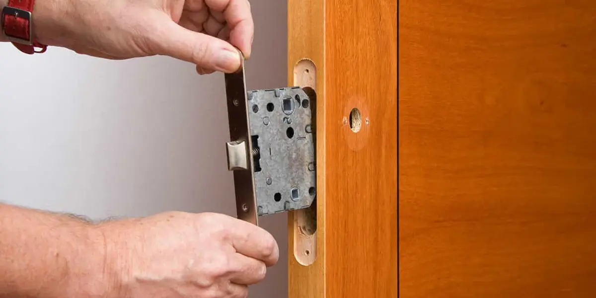 Un serrurier installe une serrure encastrée dans une porte en bois à l’aide d’un tournevis.
