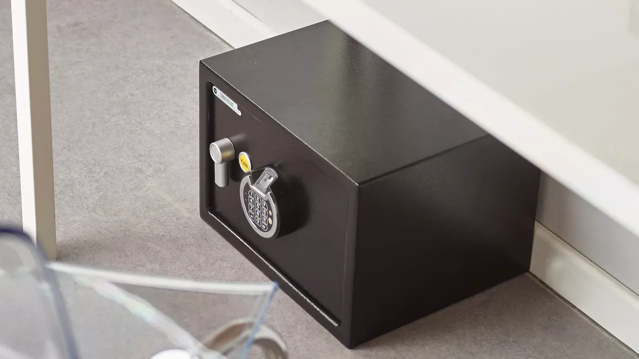 Coffre-fort électronique noir avec clavier numérique et clé, placé sous un bureau — sécurité et protection des objets de valeur par un serrurier.